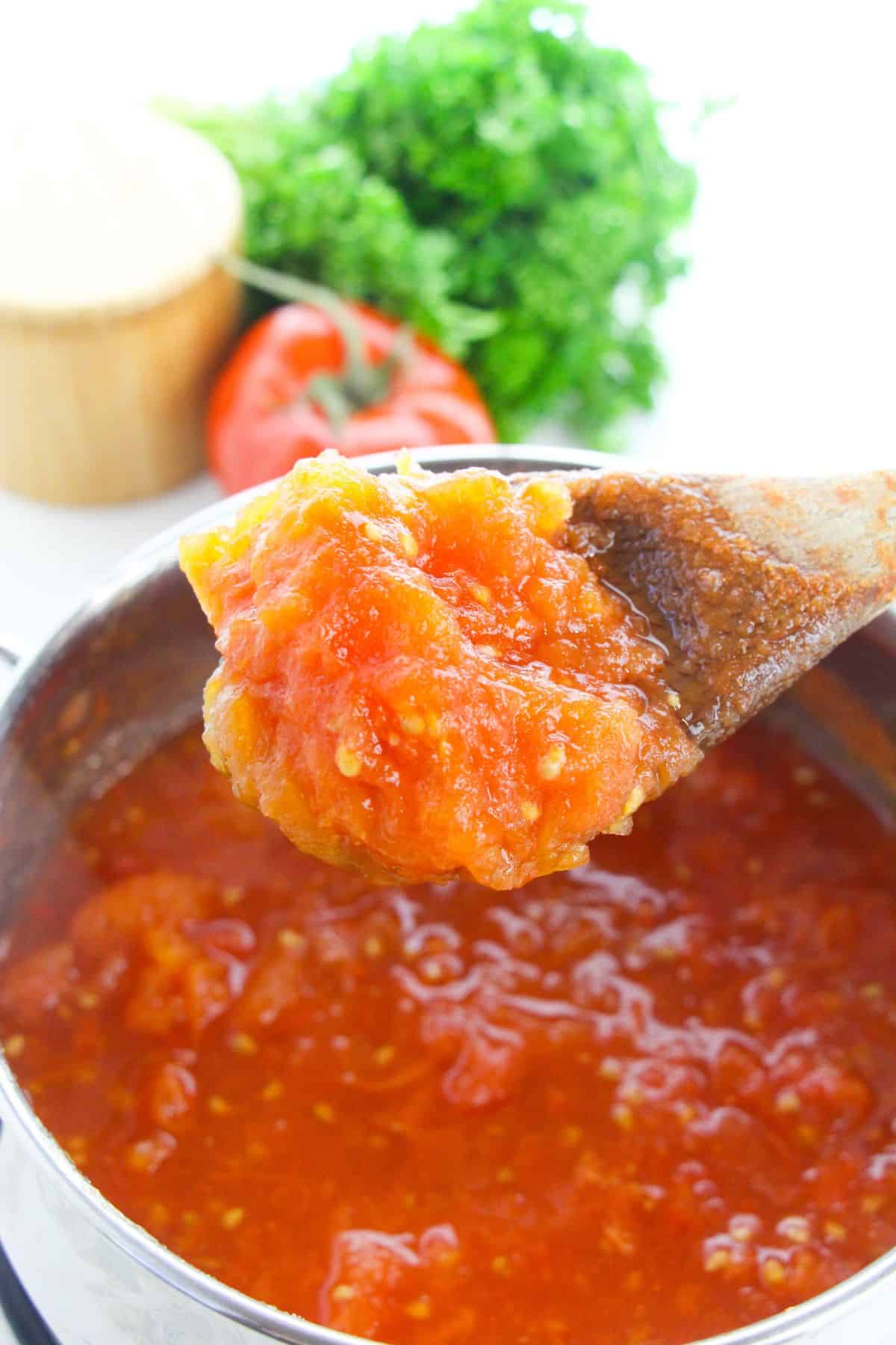 A wooden spoon with stewed tomatoes on it.