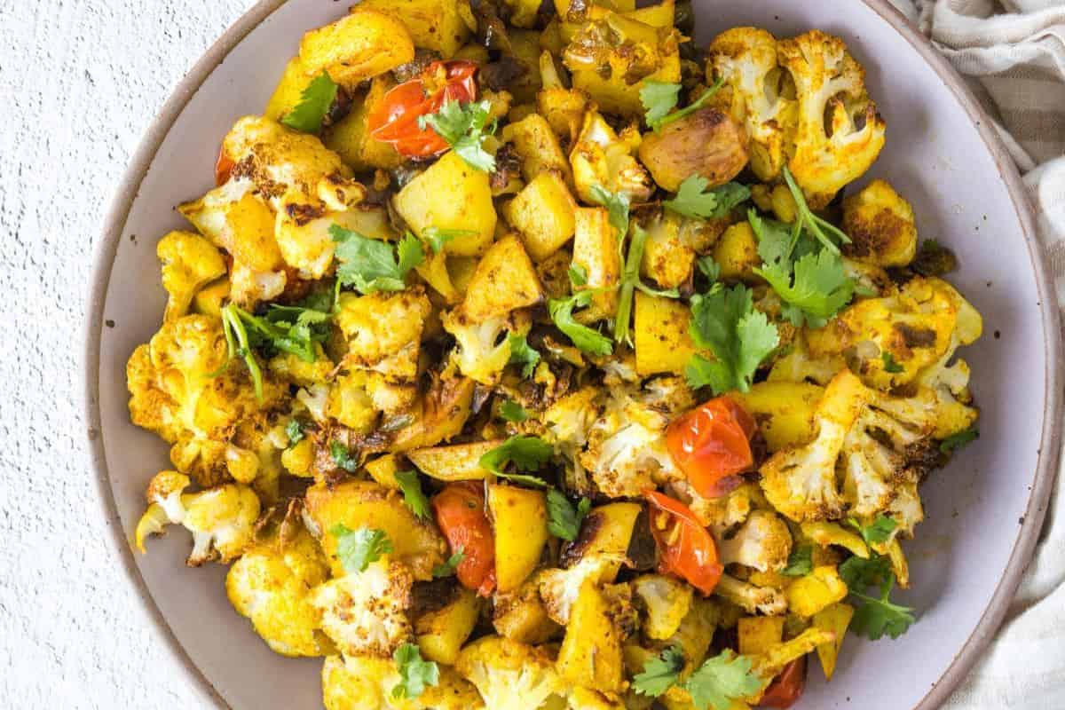 A bowl of roasted cauliflower, potatoes, tomatoes, and fresh cilantro bursts with bold flavors.