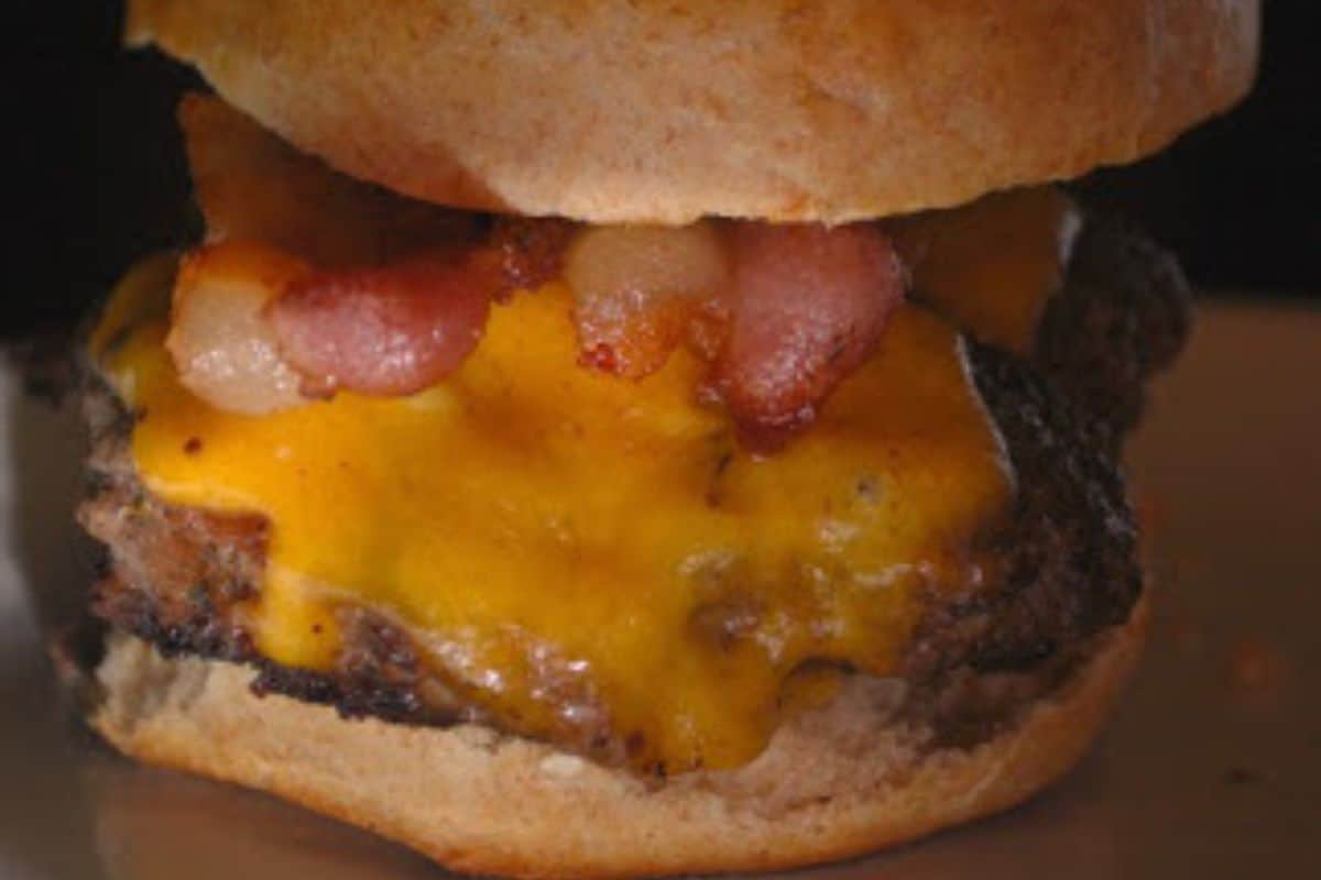 Close-up of a savory burger with melted cheddar cheese, crispy bacon strips, and a beef patty in a toasted bun—perfect inspiration for your next burger recipes.