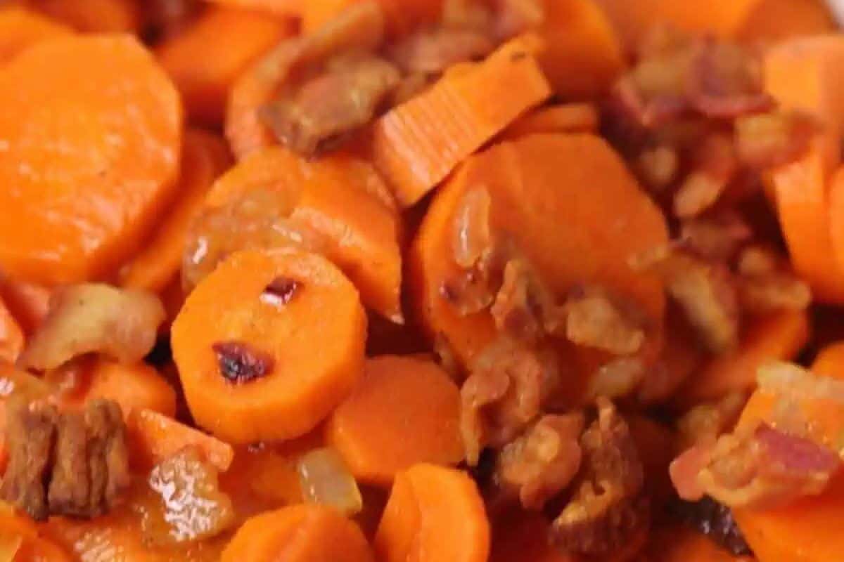 Close-up of sliced cooked carrots mixed with crispy bacon bits, showcasing a glossy glaze and rich orange and brown hues.