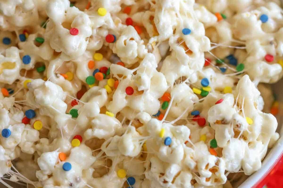 An overhead view of popcorn in a bowl with marshmallow strands and rainbow sprinkles 