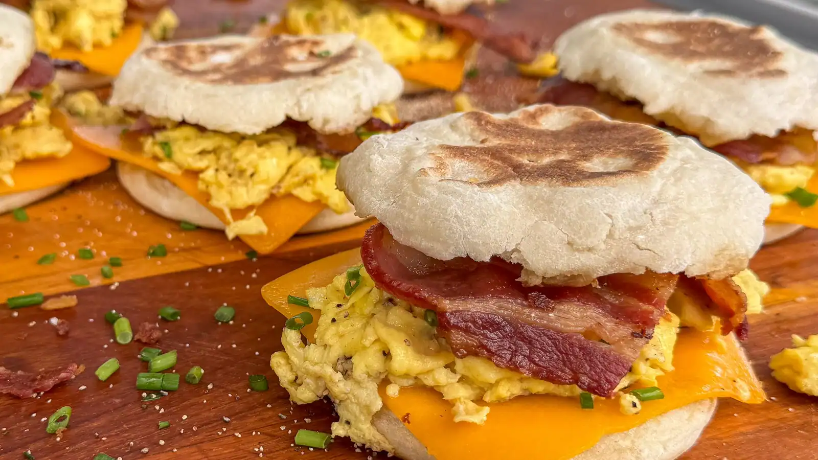 English muffins filled with scrambled eggs, cheddar cheese, bacon, and chopped chives make perfect griddle recipes for breakfast, beautifully arranged on a wooden board.