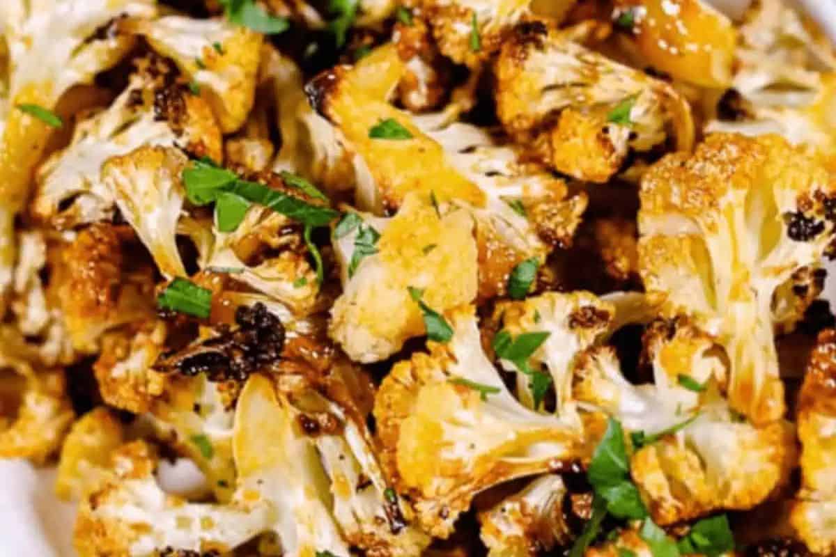 Flavor-packed roasted cauliflower florets garnished with chopped fresh herbs on a white plate.