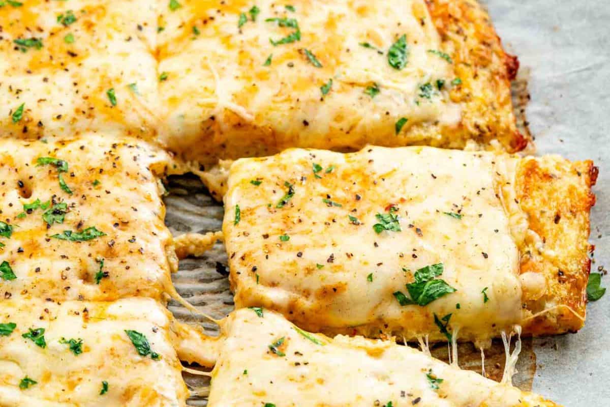 Close-up of flavor-packed cheesy bread slices topped with melted cheese, herbs, and black pepper, with one slice being pulled away.