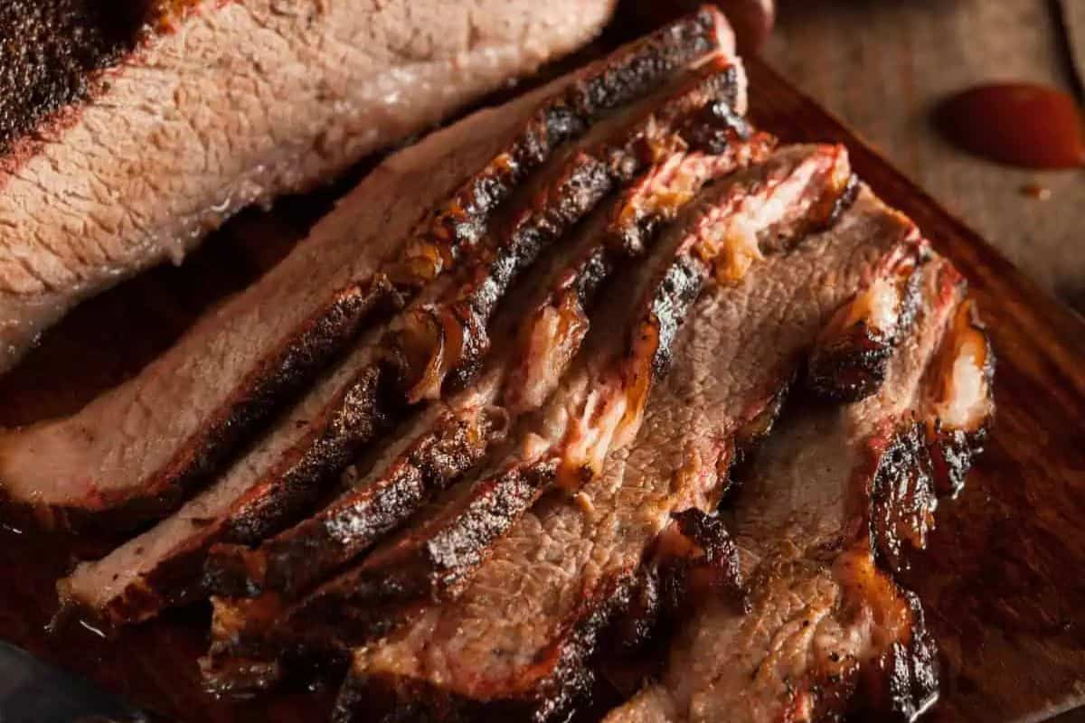 Sliced smoked brisket with a dark, caramelized bark and juicy, tender interior, arranged on a wooden cutting board.