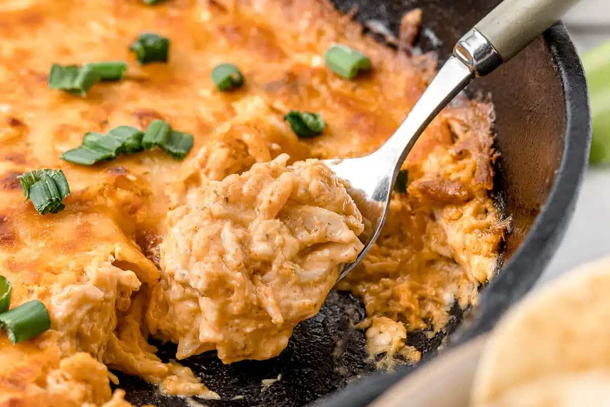 Creamy buffalo chicken dip topped with melted cheese, featuring chunks of shredded chicken, served hot in a baking pan.