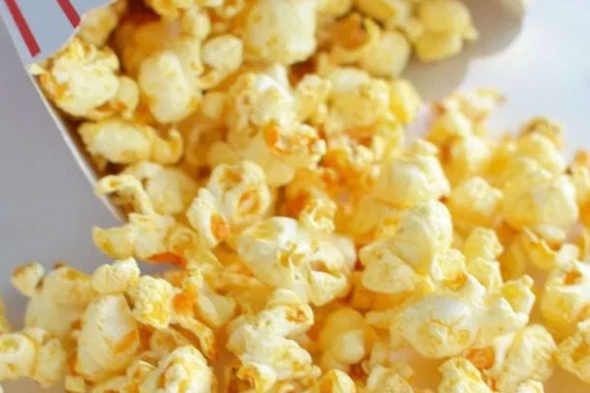  A close-up shot of fluffy popcorn seasoned with an orange-red spice blend, spilling out of a red and white striped popcorn bag onto a white surface.