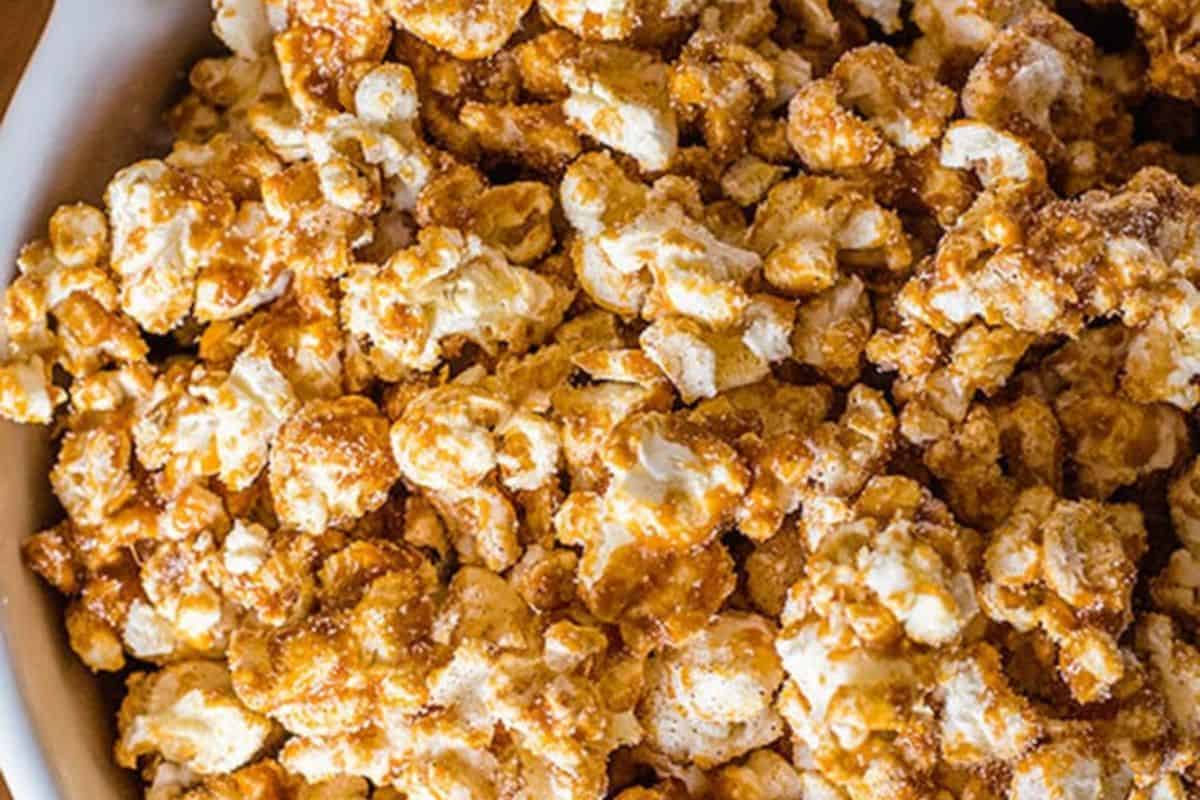 An overhead, close-up view of a bowl filled with churro-flavored popcorn, coated in a light brown, sugary, and spiced mixture.
