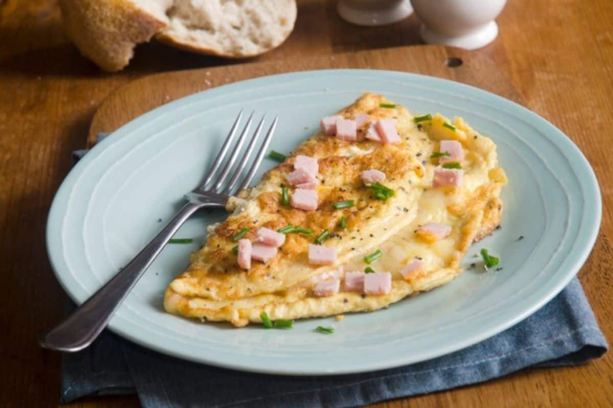 A close-up of a golden-brown omelette with visible chunks of green bell pepper, onions, and diced meat. The omelette is garnished with finely chopped green herbs.