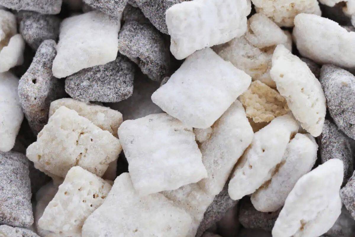 Cookies and cream muddy buddies coated in powdered sugar, featuring a mix of cereal pieces and crushed chocolate sandwich cookies for a sweet, crunchy treat.