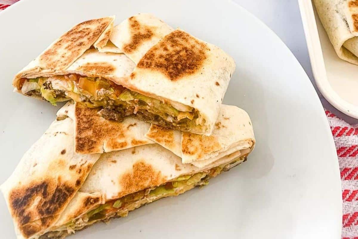 Crispy grilled crunch wraps filled with seasoned beef and melted cheese, served on a white plate.