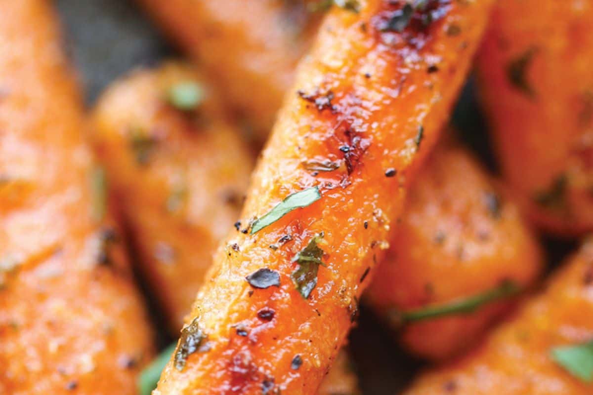 Roasted baby carrots seasoned with herbs and black pepper, glistening with oil and slightly charred for a caramelized finish.