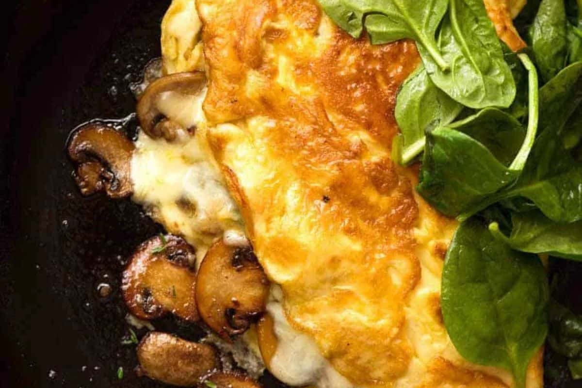 A close-up of a savory dish featuring a folded golden-brown omelette with visible ingredients such as diced vegetables and possibly ham. The omelette is garnished with small green herbs.