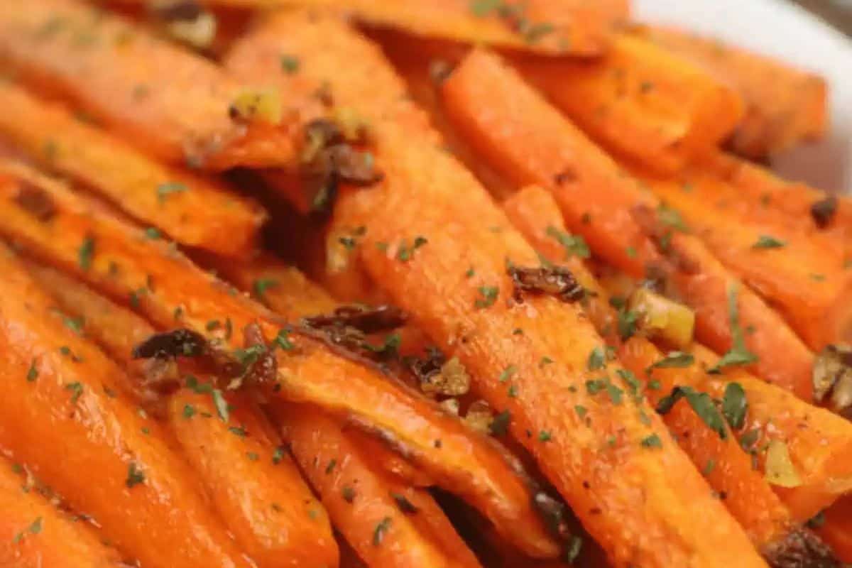 A close-up of roasted carrot sticks, glistening and seasoned with what appears to be garlic and herbs.