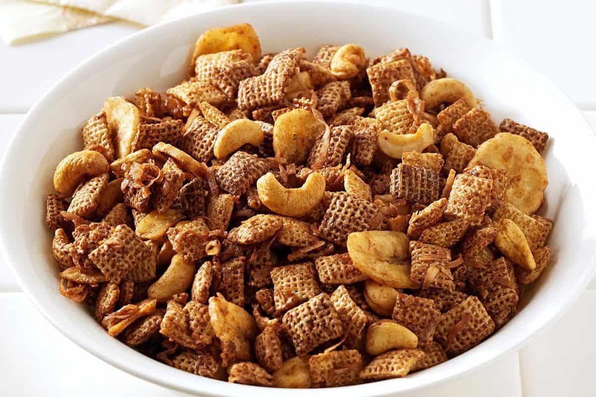 A blend of gluten-free pretzels, nuts, and chocolate candies in a white bowl.