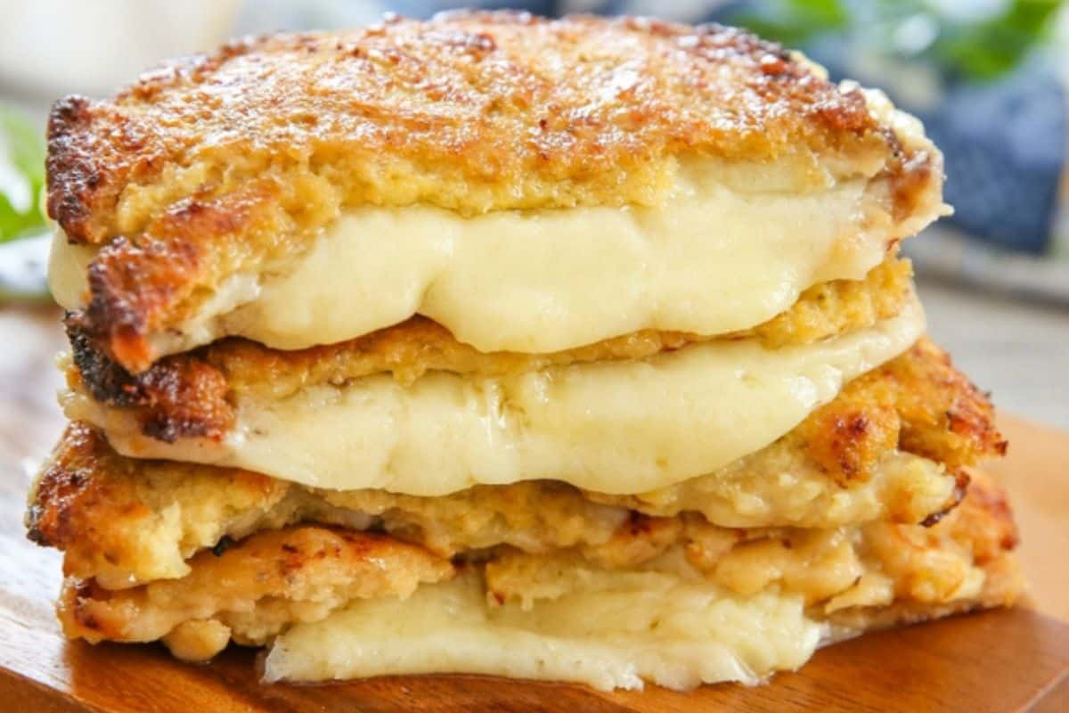 Three stacked pieces of flavor-packed grilled cheese sandwich with melted cheese oozing between golden-brown bread slices on a wooden board.