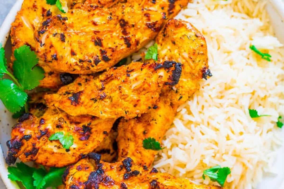 Grilled marinated chicken breast served with a side of white rice, garnished with fresh cilantro.