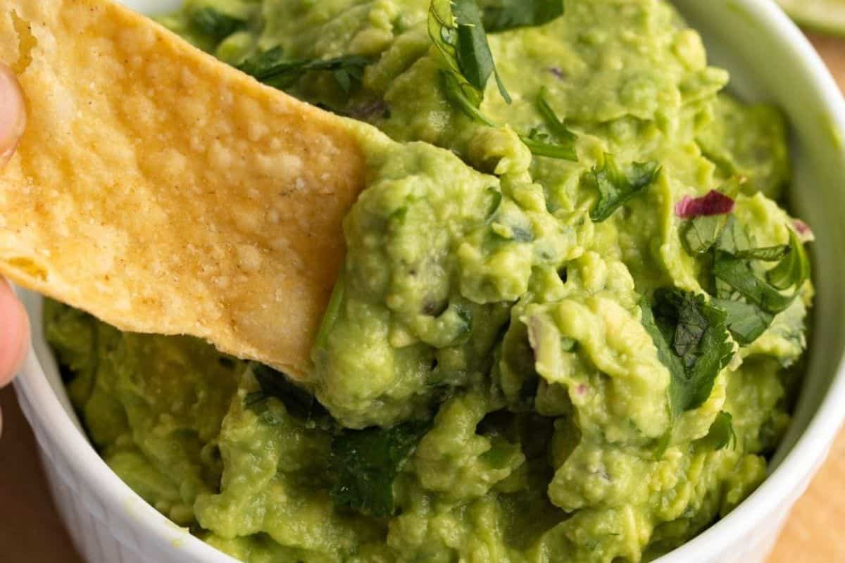 A bowl of creamy, chunky guacamole made with mashed avocados, diced tomatoes, onions, cilantro, and lime juice.