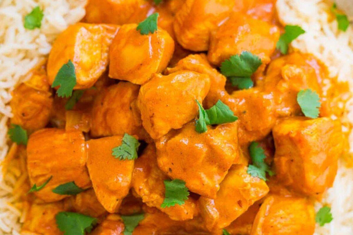 A close-up of chicken tikka masala served over rice, garnished with fresh cilantro leaves.