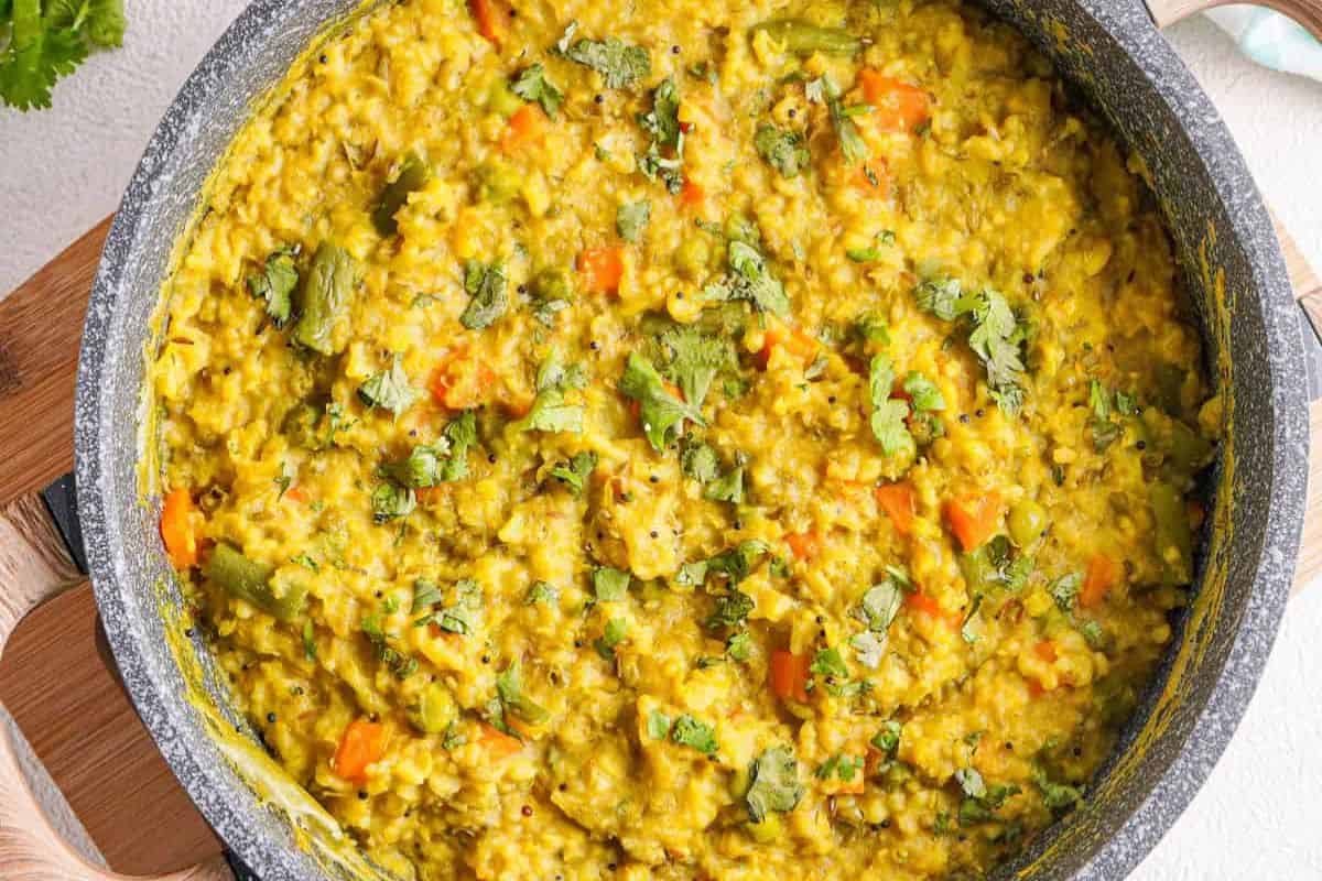 A pot filled with kitchari, a classic from Indian recipes—yellow rice and lentils mixed with veggies and garnished with fresh cilantro for bold flavors.