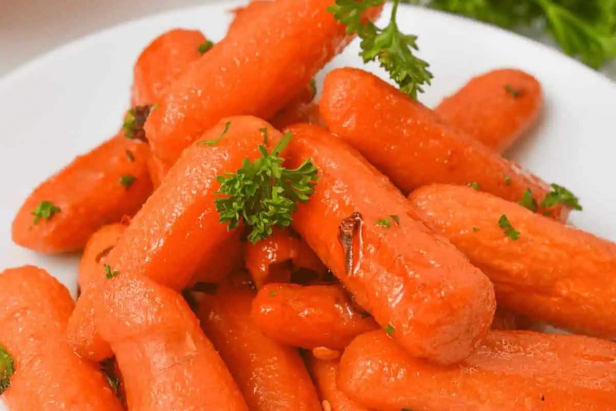 A white plate filled with whole, maple-glazed baby carrots, garnished with fresh green parsley.