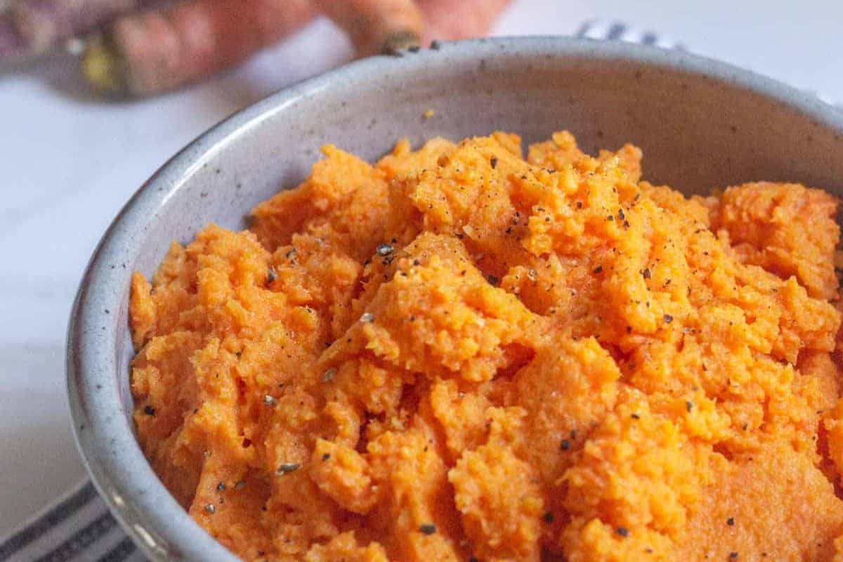 A ceramic bowl filled with a fluffy orange mashed carrot mixture, lightly sprinkled with black pepper.