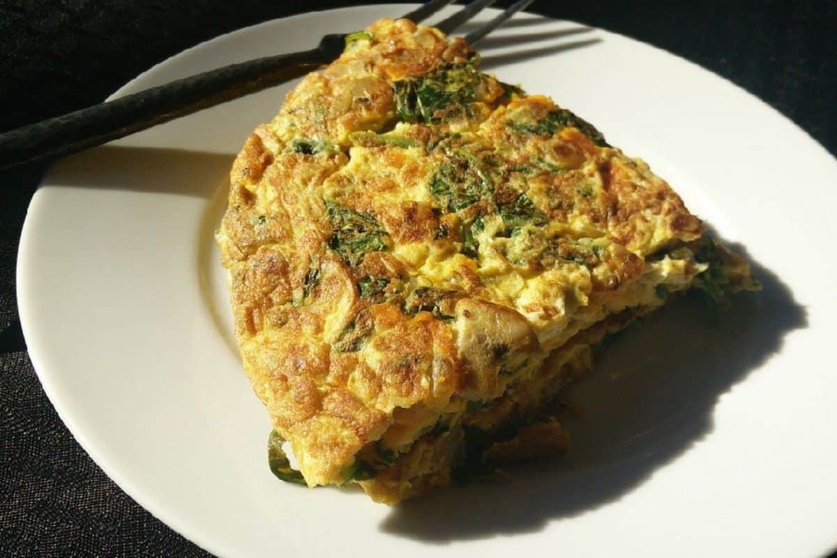 A close-up of a golden-brown omelette with a slightly crisp outer layer. The filling includes diced green bell peppers and onions, adding texture and color to the dish. The omelette is topped with finely chopped green herbs