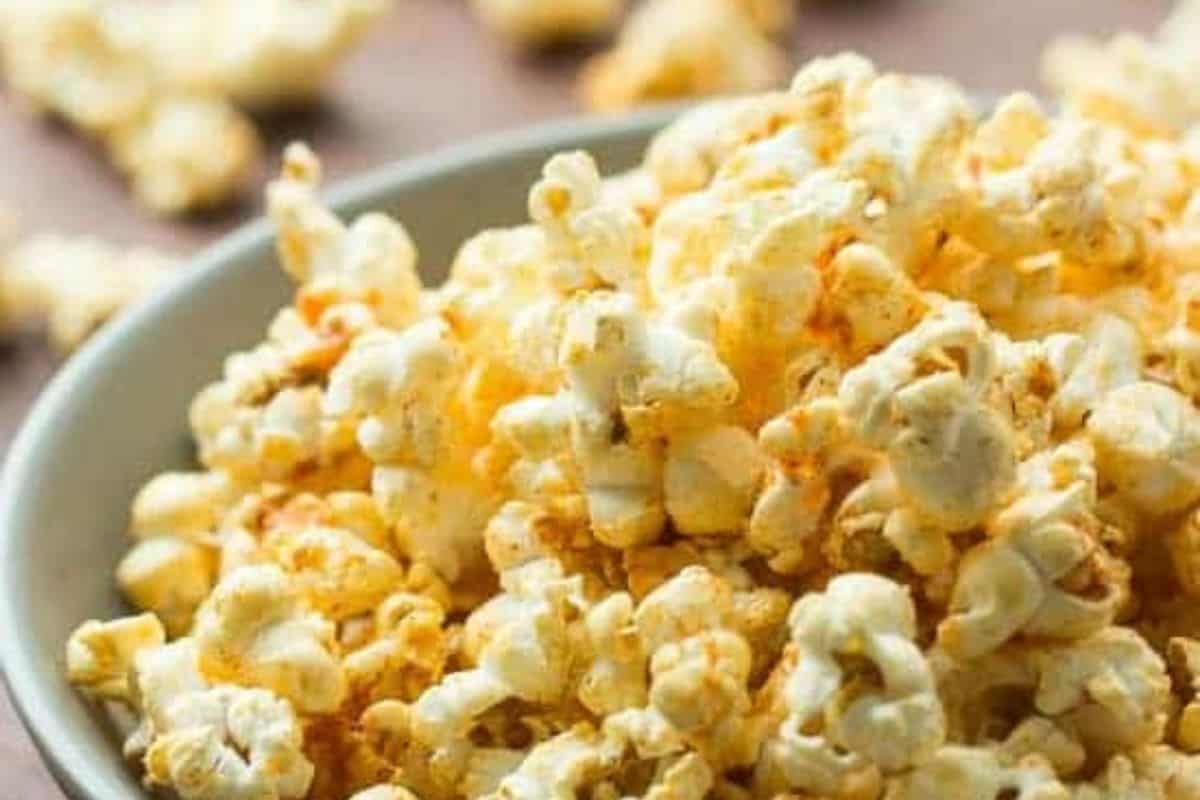  A close-up of a gray bowl filled with popcorn lightly seasoned with an orange-colored powder, likely nacho cheese flavoring. The background is blurred.