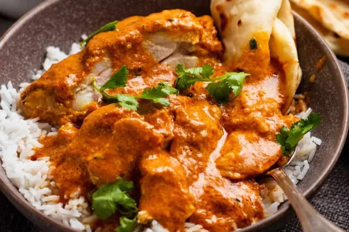 A bowl of white rice topped with chicken in orange curry sauce, garnished with cilantro and served with naan bread.
