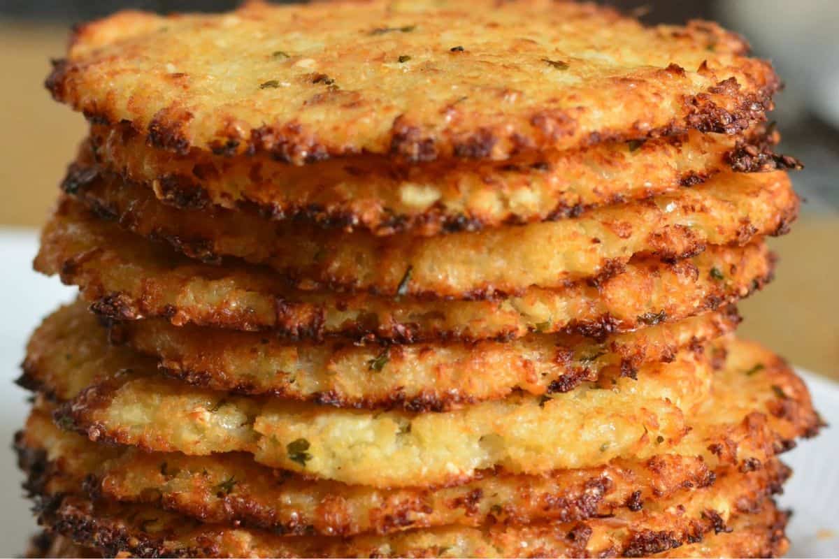 A close-up of a stack of golden-brown, crispy cauliflower fritters, showing their textured edges and specks of herbs.