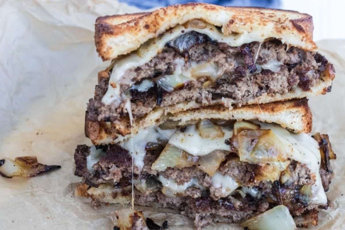 A golden-brown patty melt with melted cheese and caramelized onions, cooked on a Blackstone griddle.