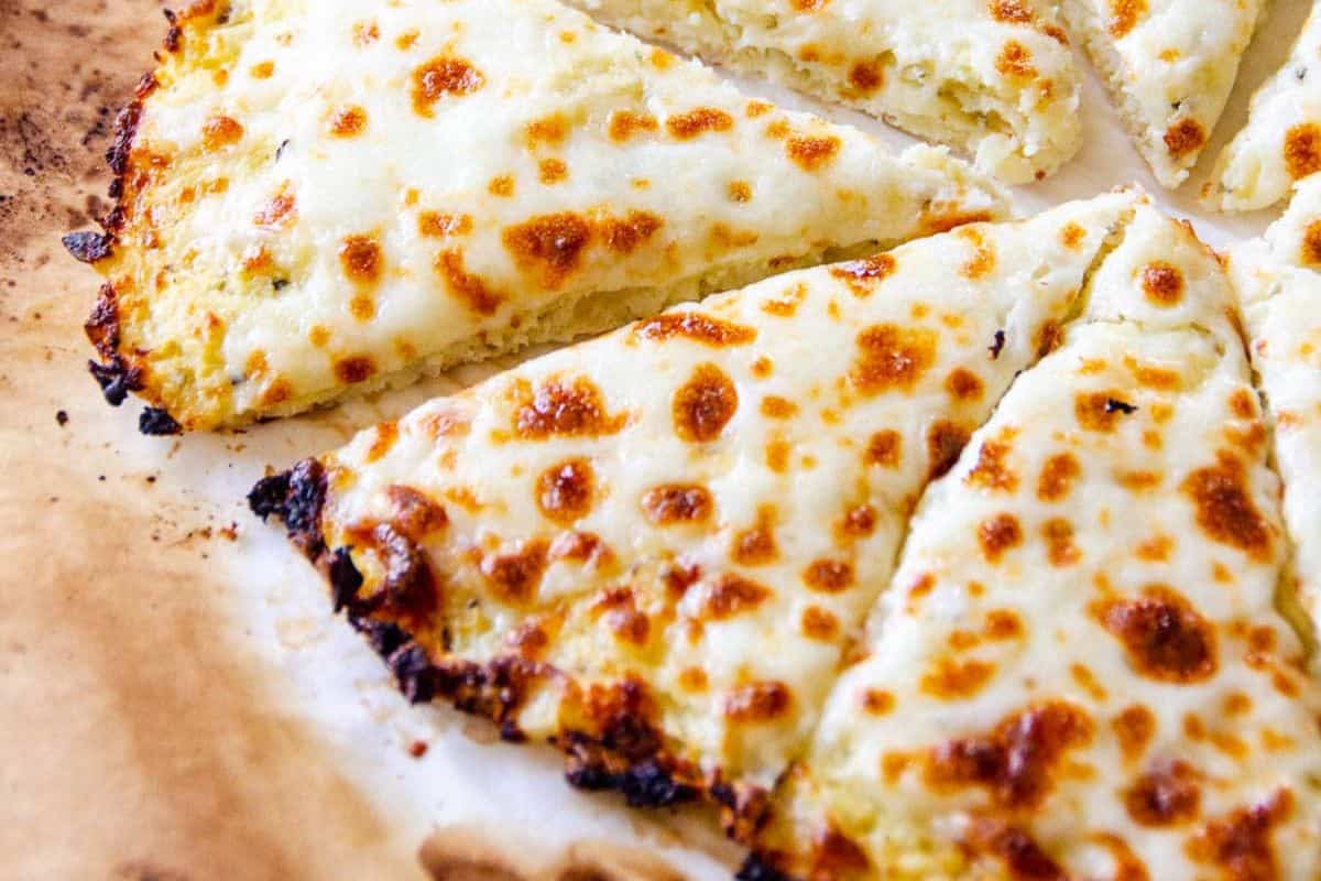 Close-up of several slices of cheesy bread with a golden, melted cheese topping on a parchment-lined surface.
