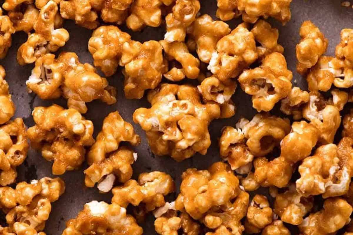 An overhead, close-up view of a pile of golden-brown salted caramel popcorn spread out, showing individual kernels coated in the sticky, sweet caramel.