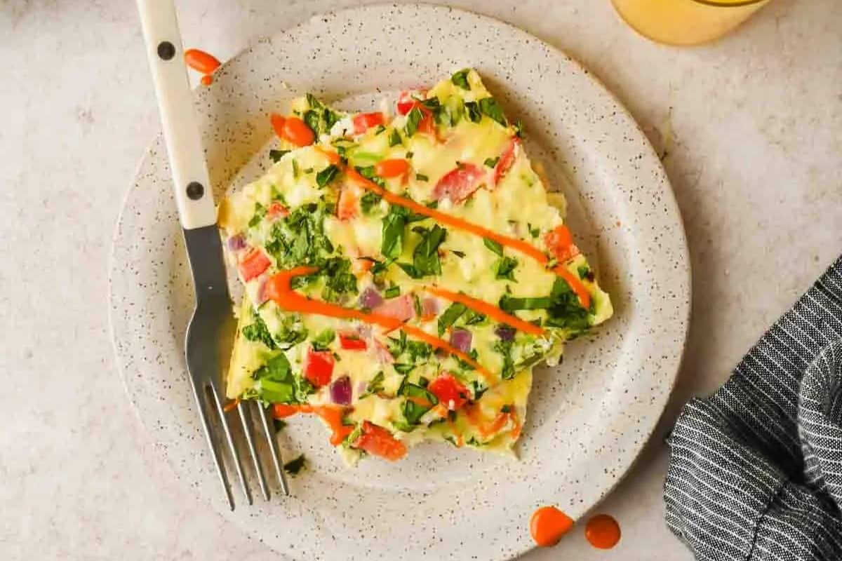 A close-up of a golden-brown omelette filled with diced vegetables and possibly ham or sausage. The omelette is garnished with finely chopped green herbs.