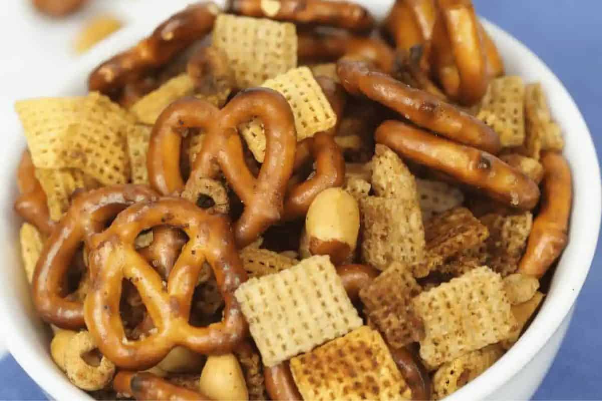 Bowl filled with slow cooker party snack mix including pretzels, Chex cereal, peanuts, and seasoned crunchy bits.