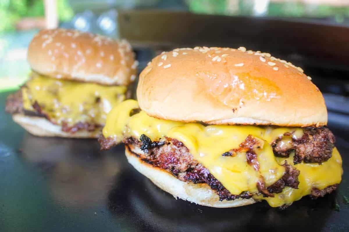 Juicy burgers with buns cooking on a Blackstone griddle.