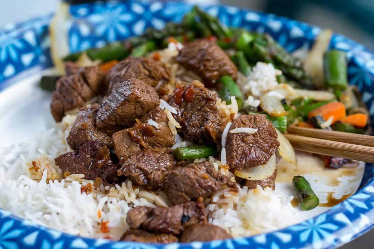 A bowl filled with steak bites served over rice and mixed vegetables.