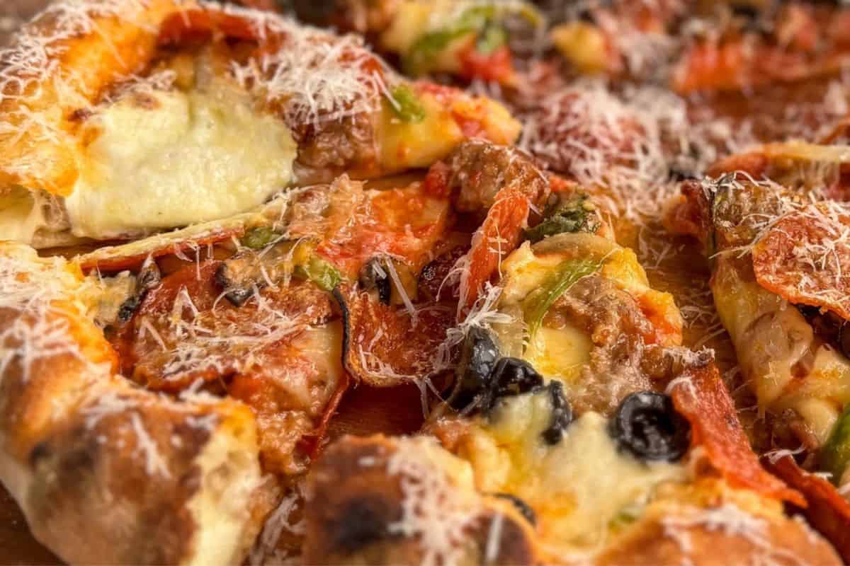 A close-up of stuffed crust pizza with melted cheese oozing from the crust and a savory topping layer.