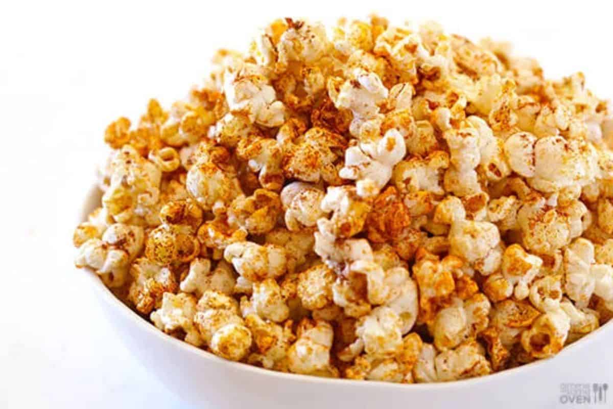 A white bowl brimming with popcorn that is heavily seasoned with an orange-brown spice blend, likely taco seasoning, set against a white background.