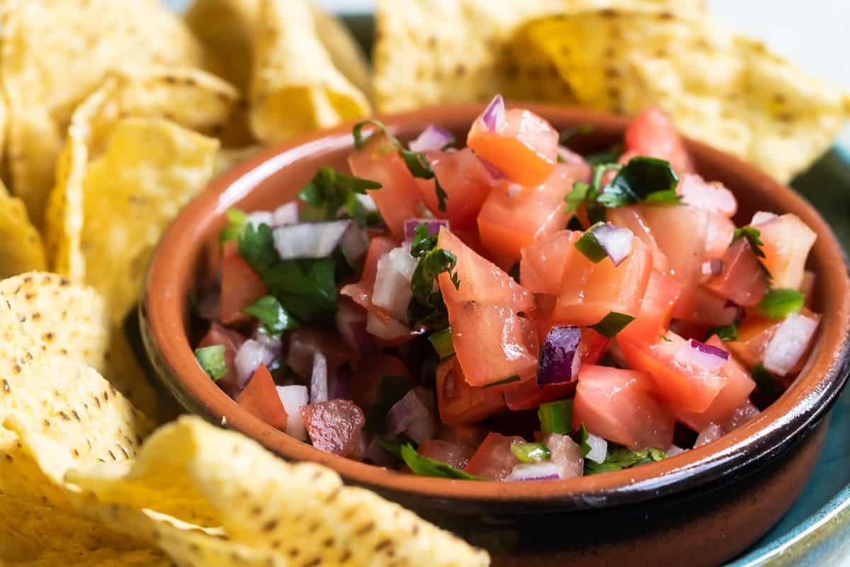 A vibrant bowl of fresh tomato salsa with diced red tomatoes, onions, jalapeños, cilantro, and lime juice, bursting with color and texture.