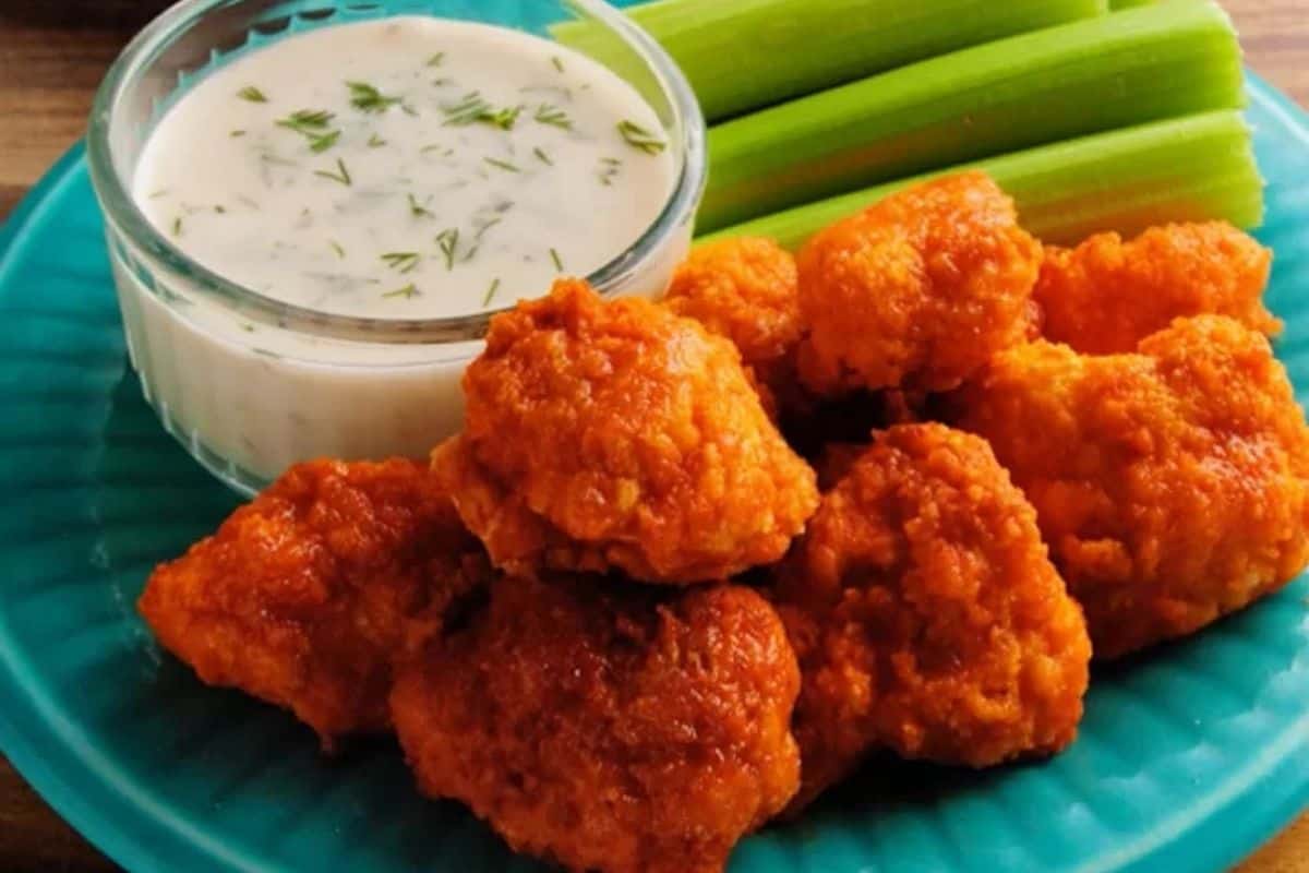 A flavor-packed plate of buffalo cauliflower bites with ranch dip and celery sticks on a blue plate.