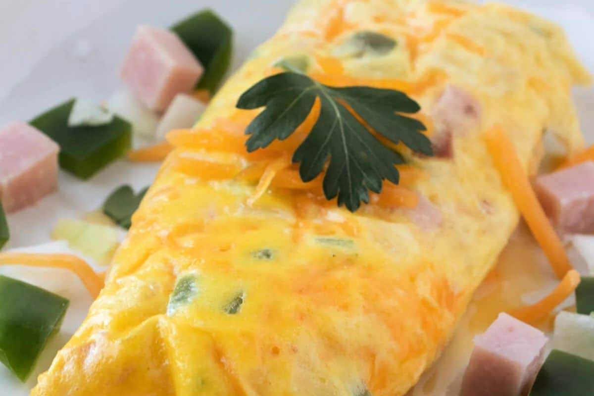 A close up of an omelette with cheese ham and topped with a garnish 