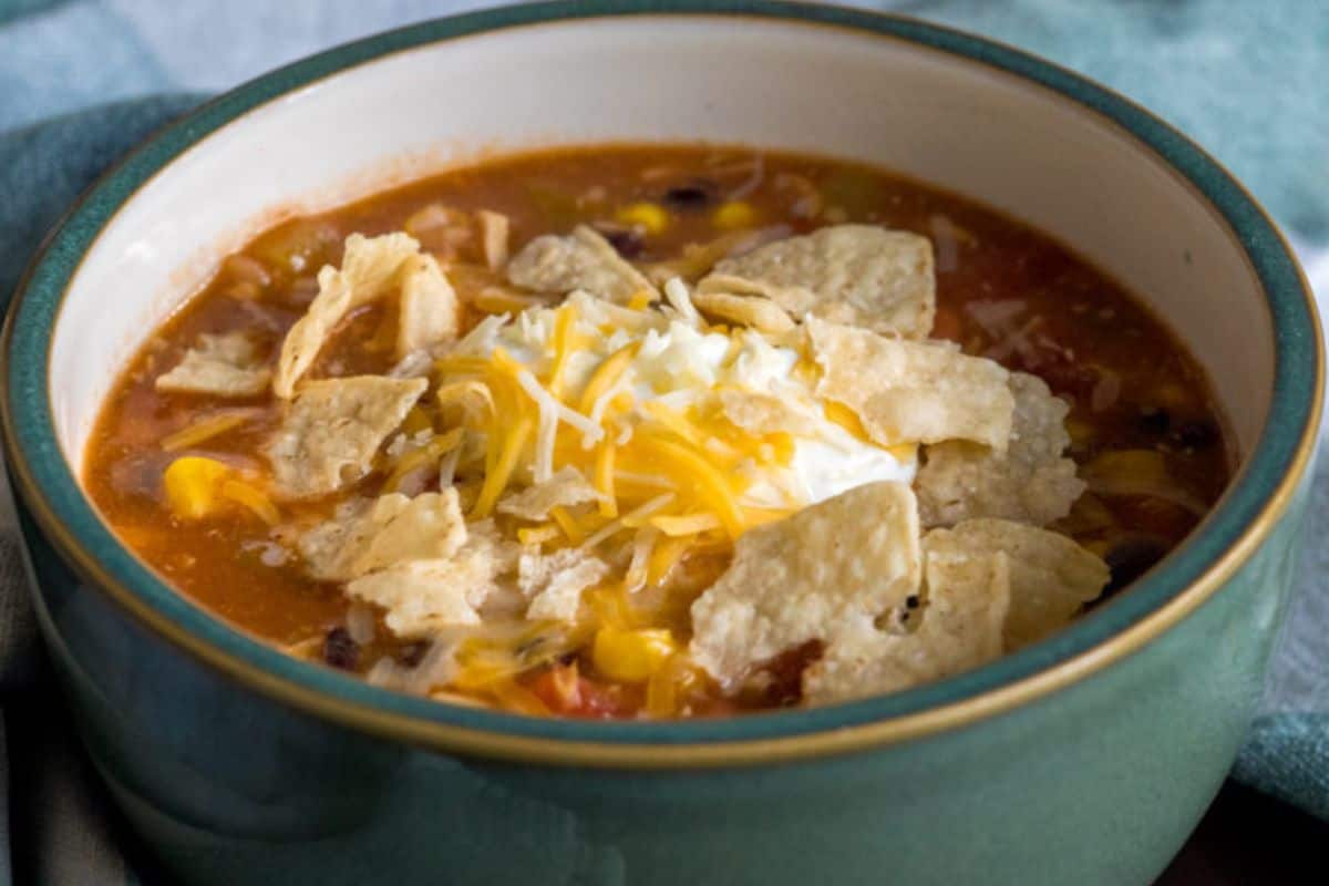 A bowl of chicken taco soup topped with shredded cheese, sour cream, and crumbled tortilla chips—one of our favorite budget friendly dinners made even easier with canned chicken.
