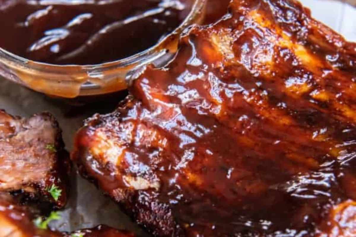 Close-up of some air fryer baby back ribs, coated in BBQ sauce and served with a side of BBQ sauce too.