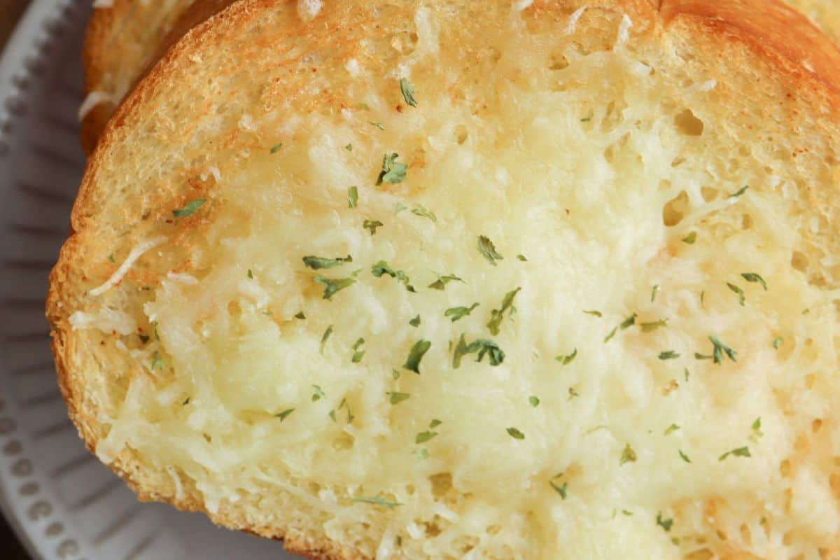 Close-up of some traditional garlic bread, topped with some white cheese and parsley flakes. Served on a light blue plate.