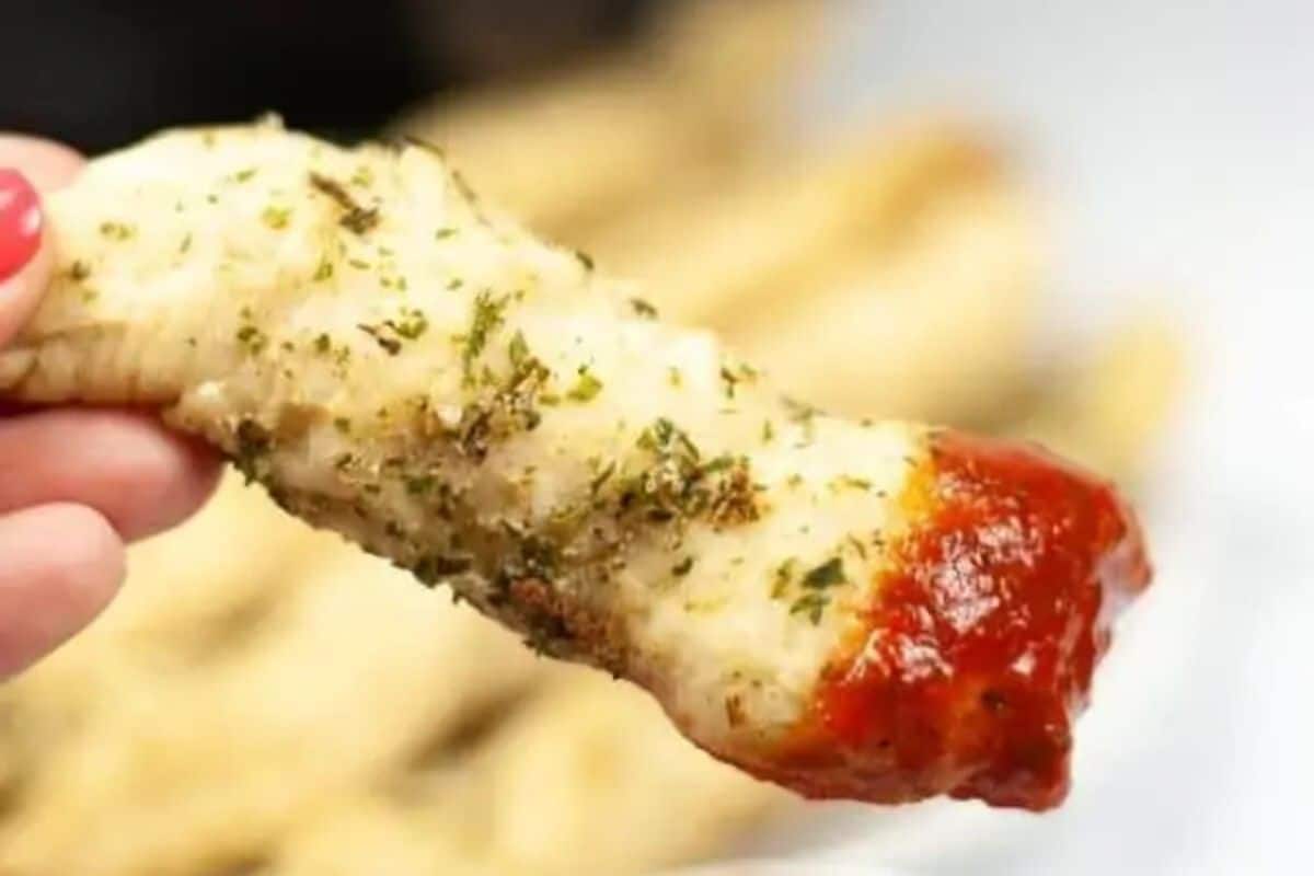 Close-up of a cheesy garlic brad stick dipped in marinara sauce. 