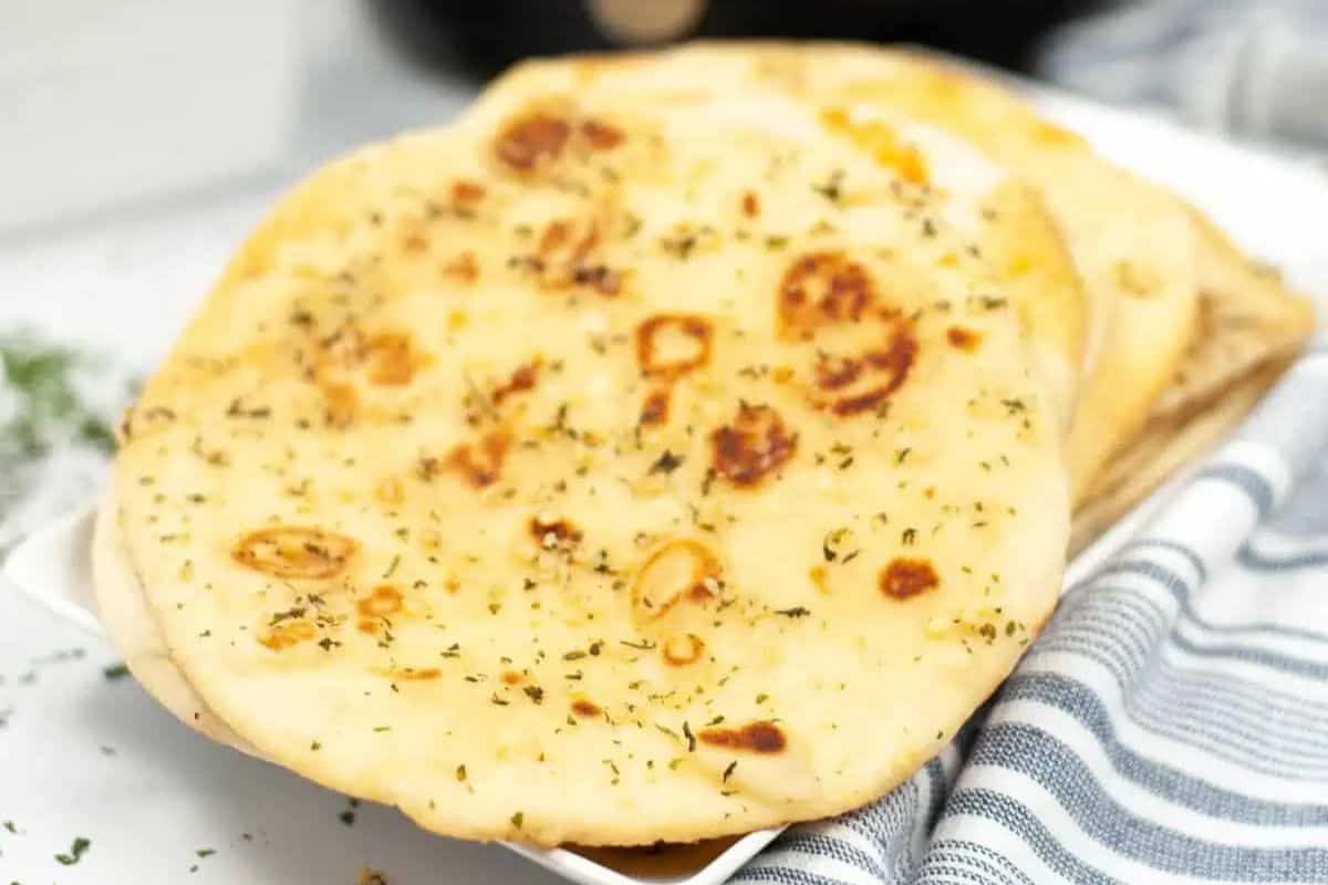 Close-up of some garlic naan bread, served on a white plate and a grey and white striped tablecloth.