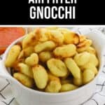 A white bowl filled with crispy, golden Air Fryer Gnocchi sits on a checkered cloth, with a small dish of red sauce in the background.