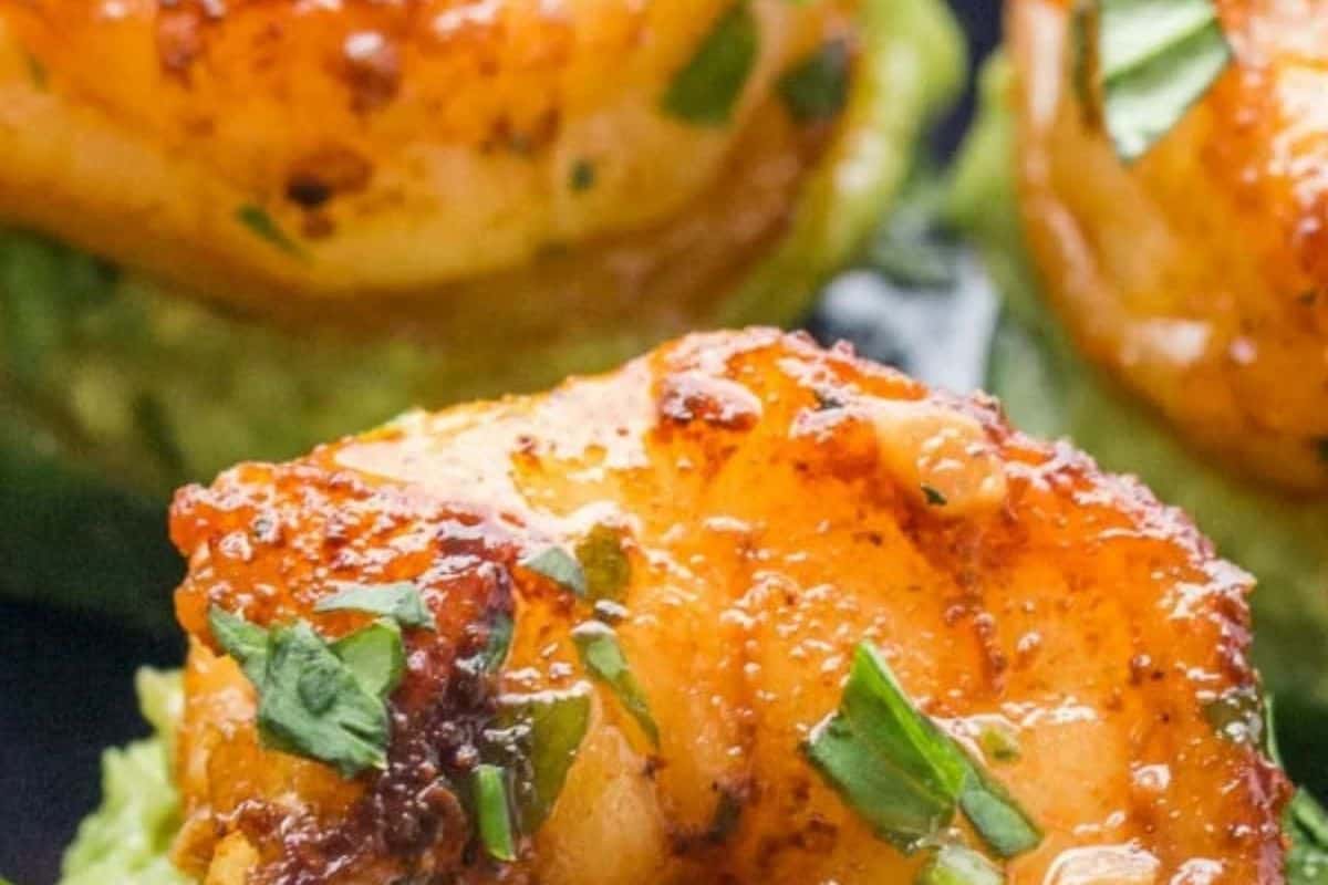 Close-up of seasoned, cooked shrimp garnished with chopped herbs, resting on a green base—possibly avocado—perfect for cold appetizer ideas.