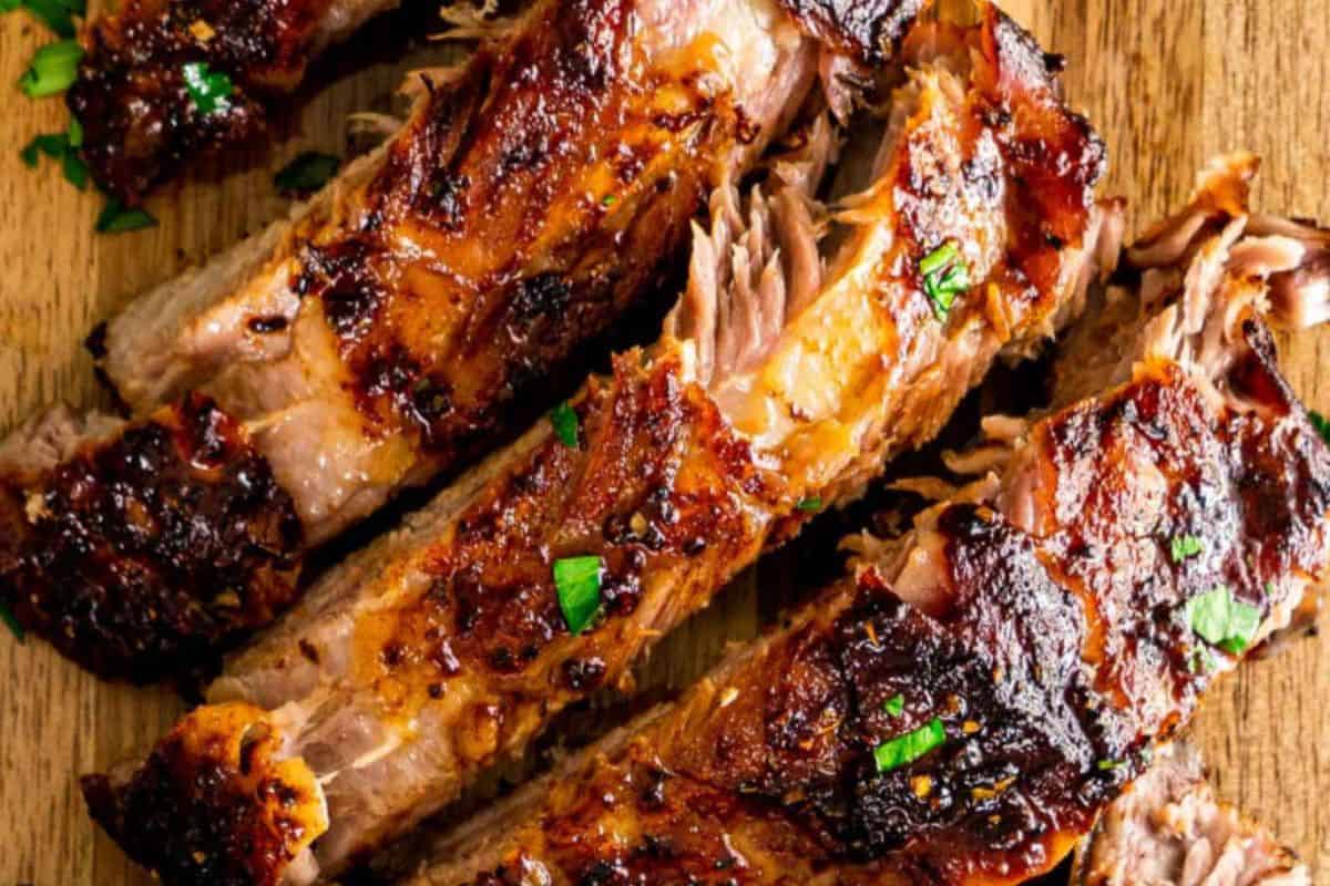 Close-up of some baked honey glazed pork ribs, pictured on a wooden cutting board.